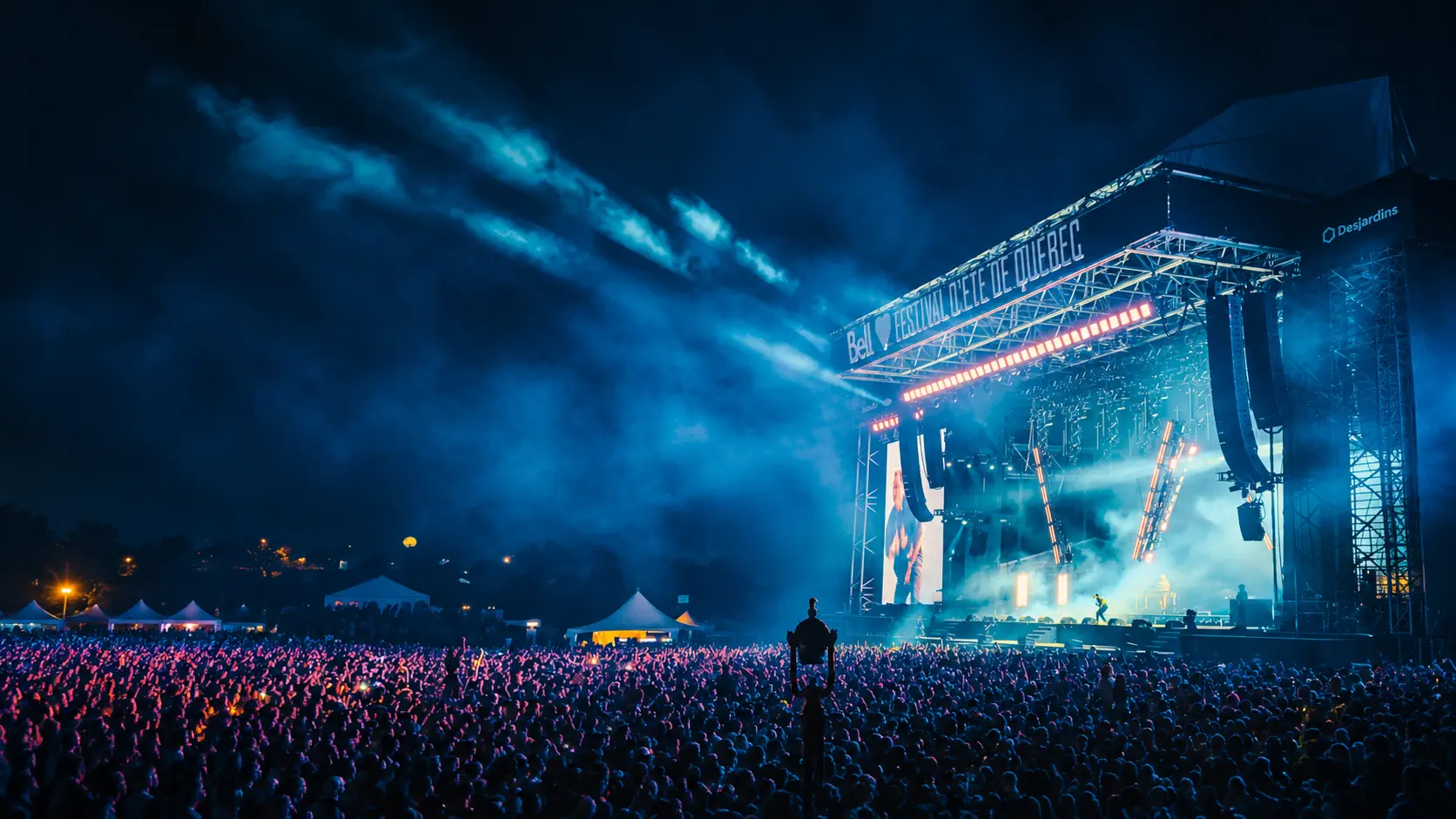 Público em show com luzes coloridas no palco.